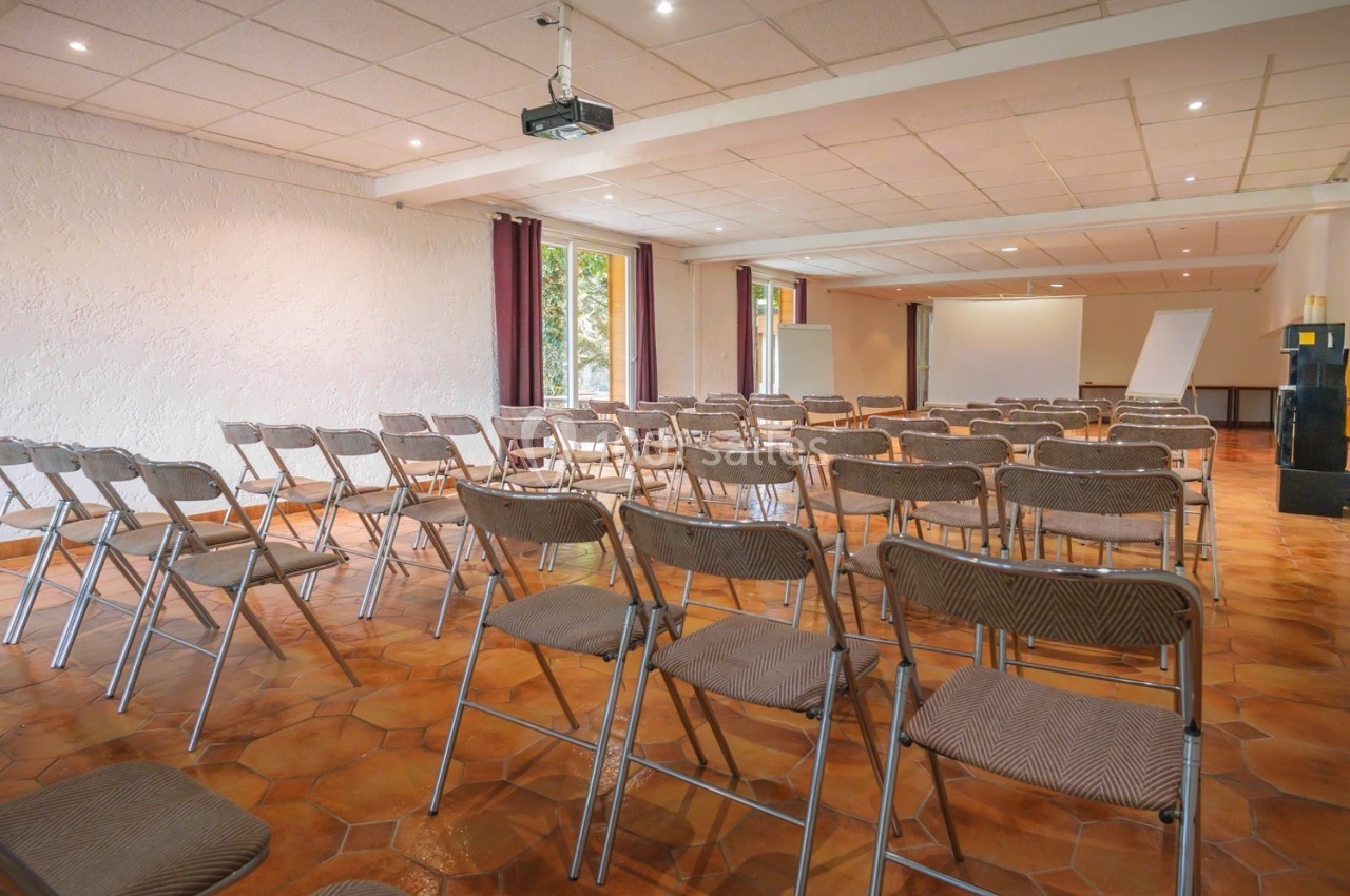 Salle de réunion lumineuse avec chaises pliantes disposées face à un écran de projection et un paperboard.