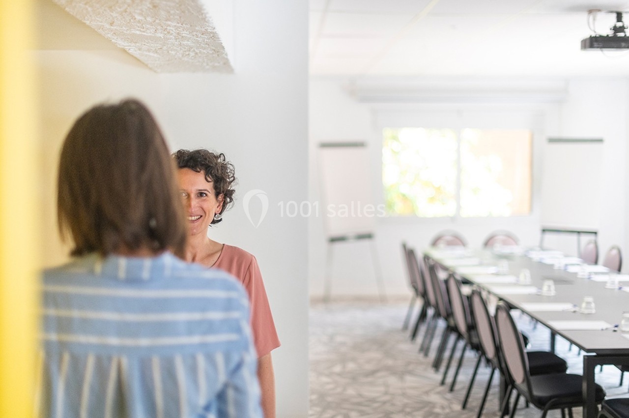 Deux femmes discutent dans une salle de réunion lumineuse avec une table de conférence et des chaises en arrière-plan.