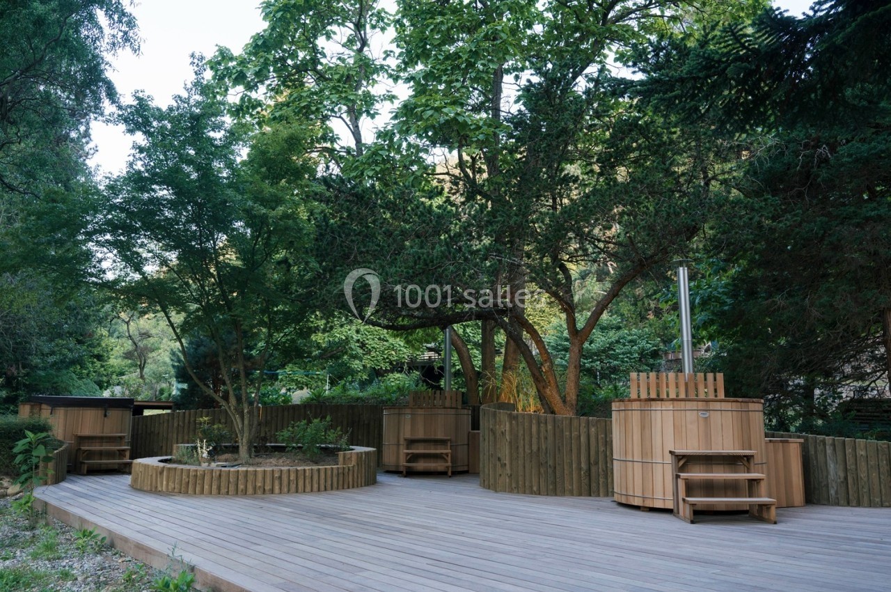 Terrasse en bois avec bains nordiques entourés d'arbres et de végétation dans un cadre naturel.