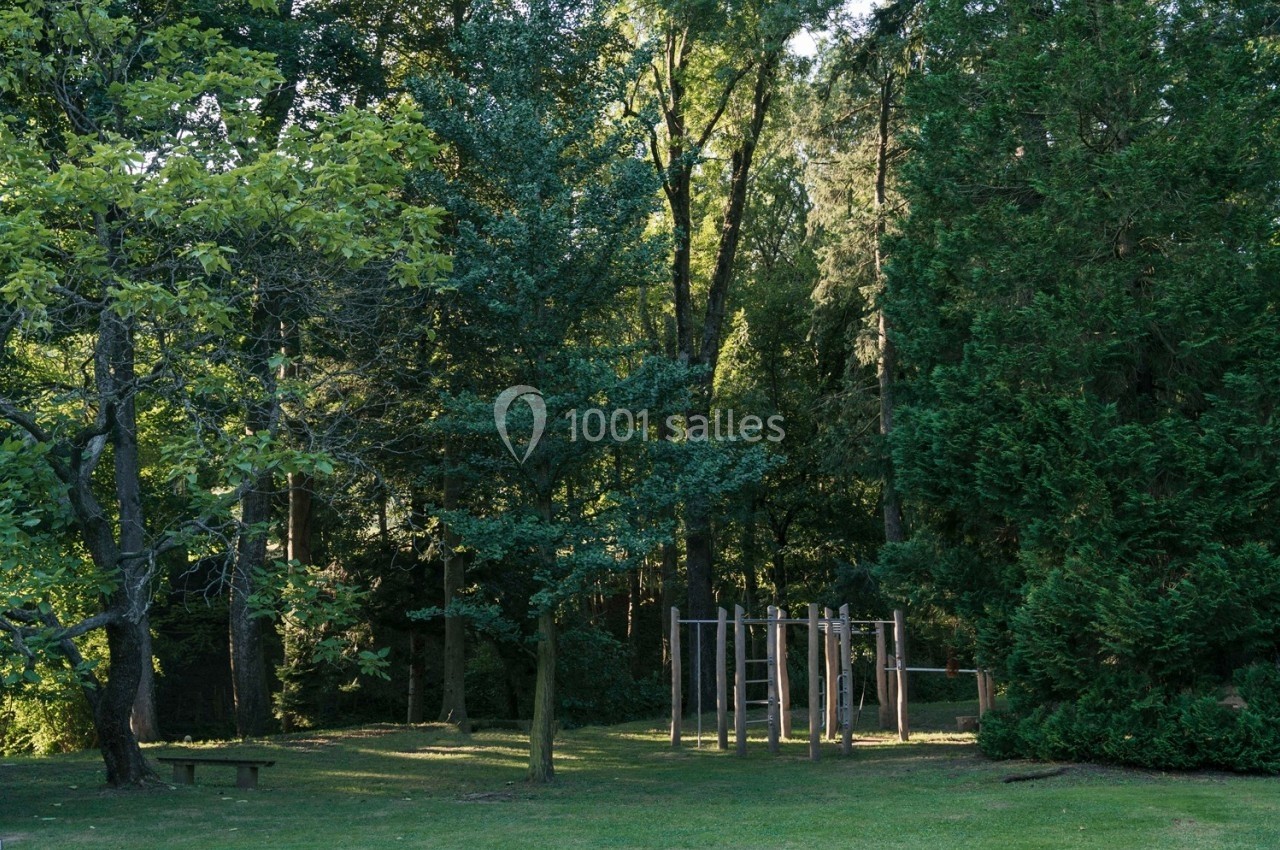 Structure en bois pour jeux d'enfants dans un parc verdoyant entouré d'arbres.