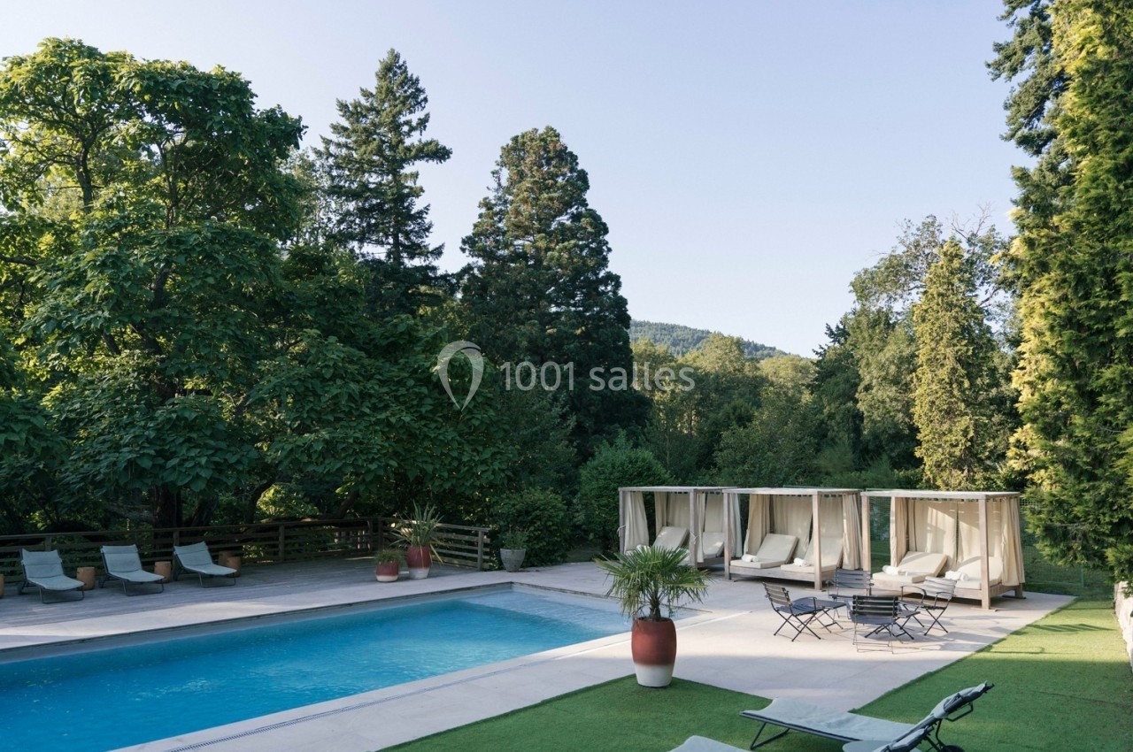 Piscine extérieure entourée de chaises longues, lits baldaquins et végétation luxuriante sous un ciel dégagé.
