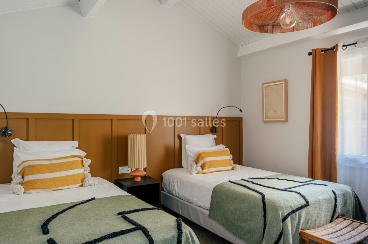 Deux lits simples avec des coussins rayés et des couvertures vertes dans une chambre lumineuse au décor épuré.