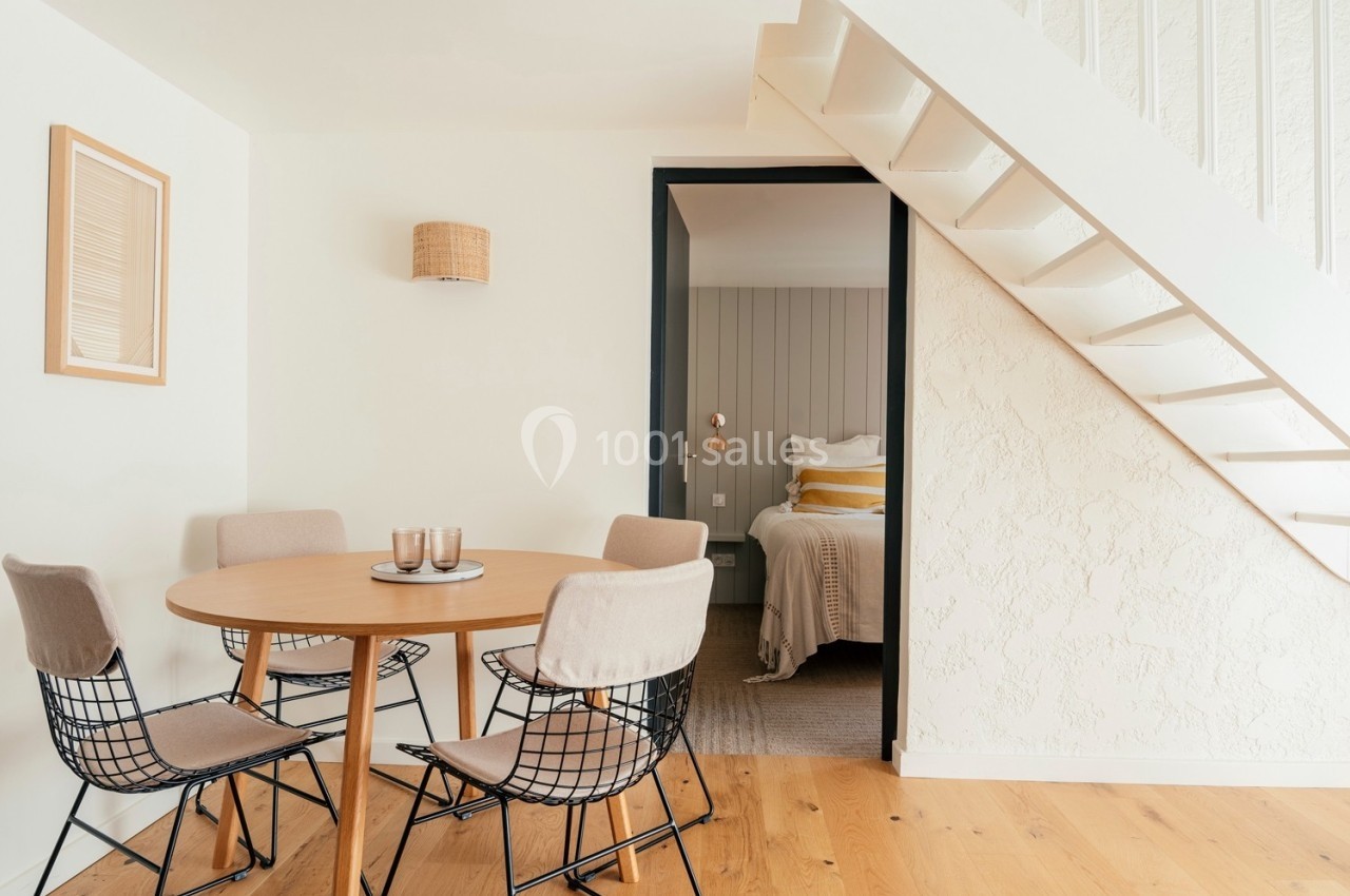 Salle à manger lumineuse avec table ronde, chaises design et vue sur une chambre à travers une porte ouverte.
