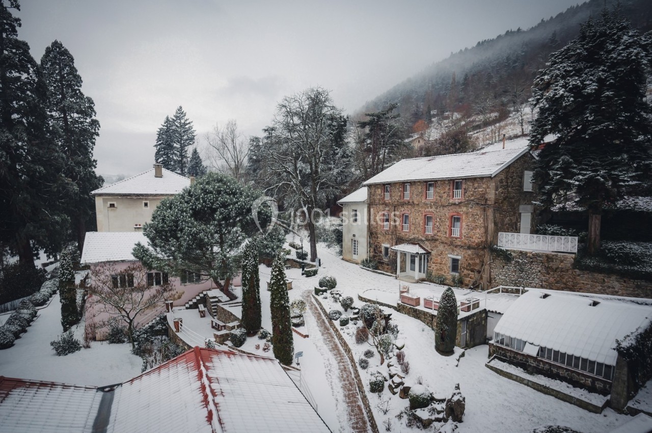 Vue d'un village enneigé avec des maisons en pierre et des toits recouverts de neige, entouré d'arbres et de collines.