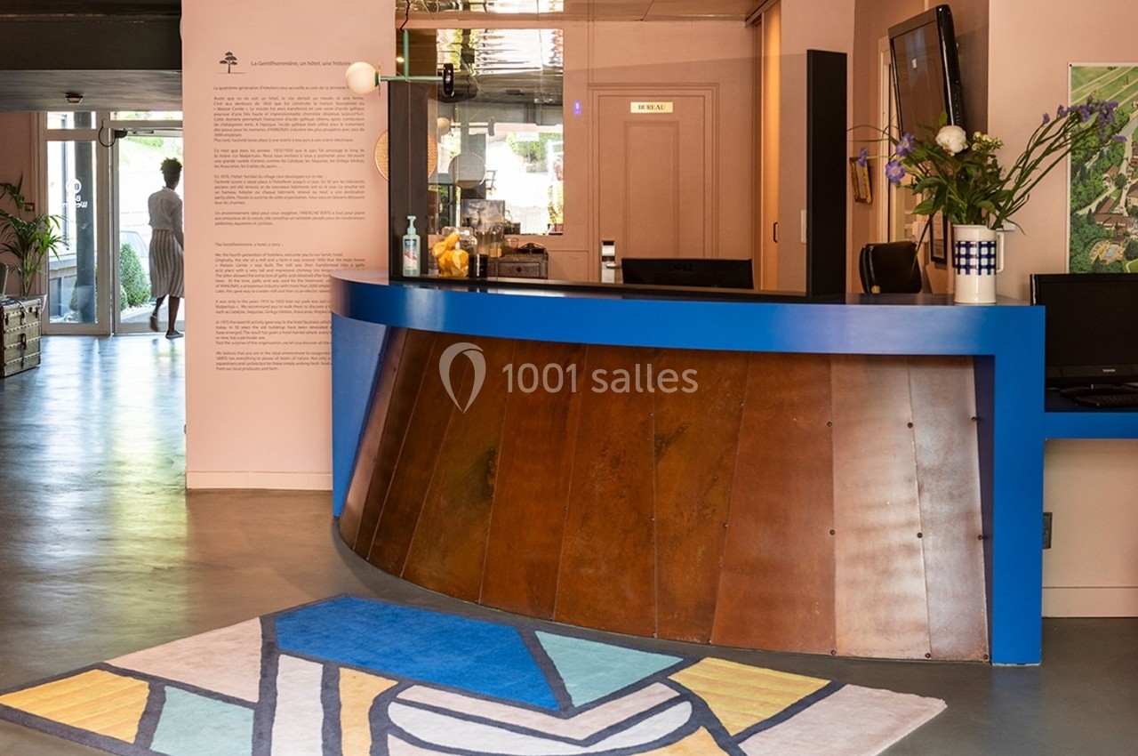 Comptoir d'accueil incurvé en bois et bleu, décoré de fleurs, avec un tapis coloré au sol dans un espace lumineux.