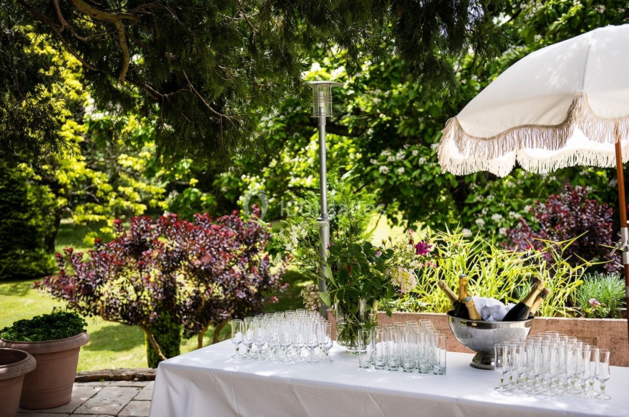 Table dressée en extérieur avec des verres à pied, un seau à champagne et un parasol, entourée de verdure.