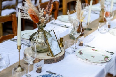 Table dressée avec nappes blanches, vaisselle vintage, chandeliers et décorations florales séchées.