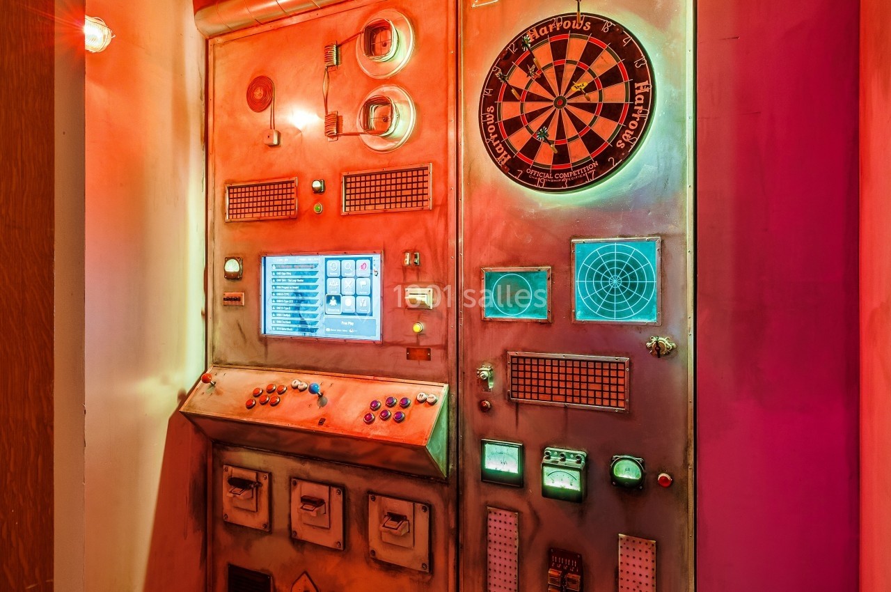 Panneau de commande rétro-futuriste avec cadrans, boutons, écrans et une cible de fléchettes éclairée.