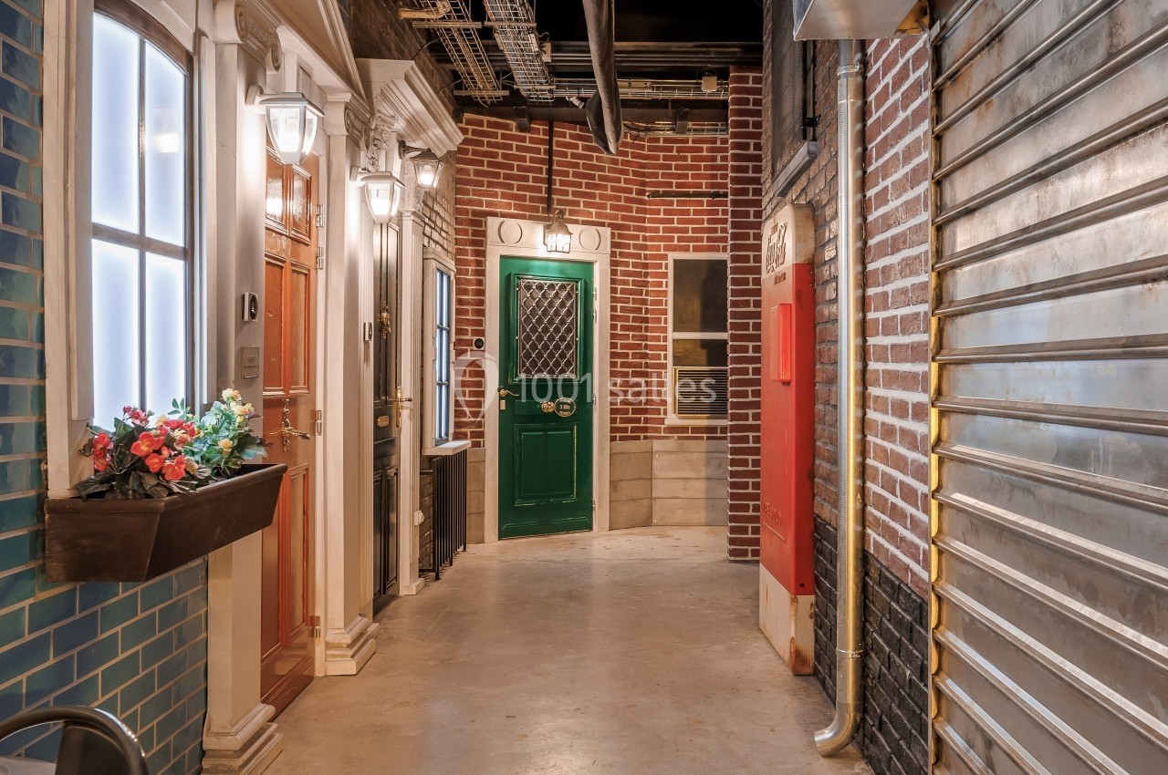 Couloir intérieur avec façades imitant des devantures de maisons, éclairage artificiel et éléments industriels visibles.