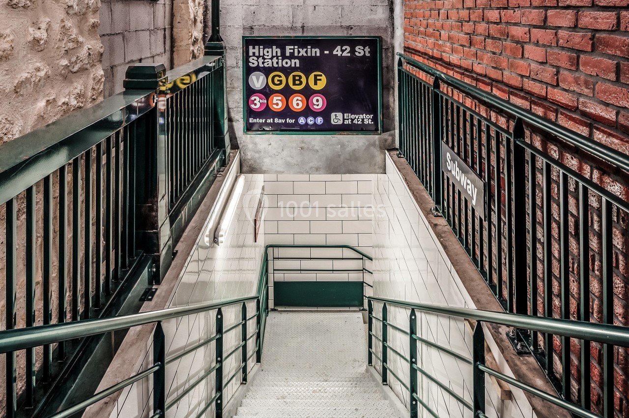 Escalier descendant vers une station de métro, entouré de murs en briques et en pierre, avec un panneau d'indications.