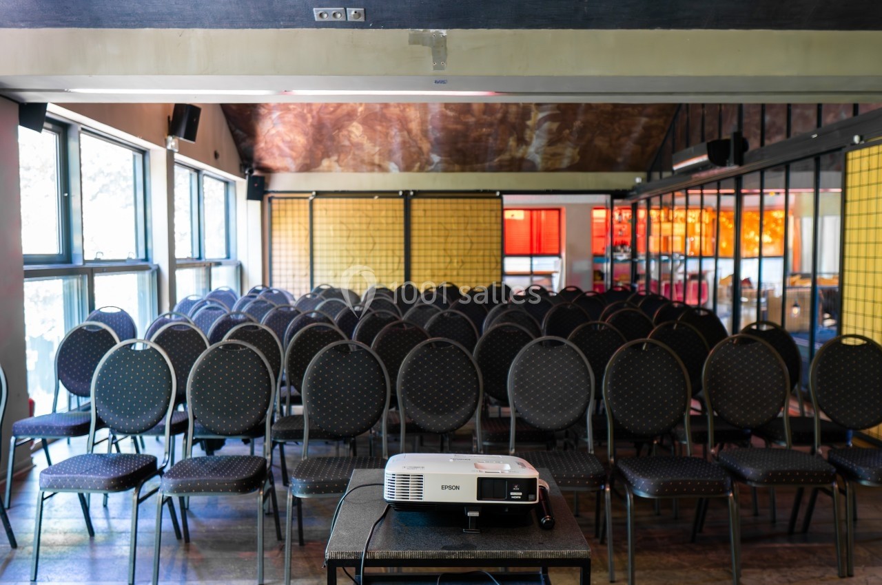 Salle de conférence vide avec des rangées de chaises alignées et un projecteur posé sur une table au premier plan.