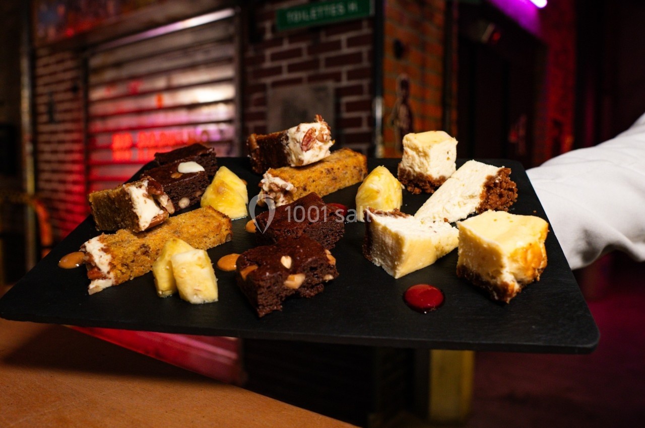 Assortiment de desserts variés, incluant brownies, cheesecake et autres pâtisseries, présenté sur une ardoise noire.