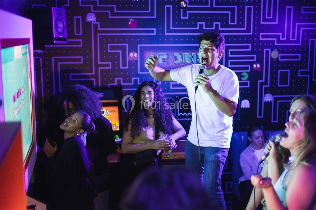 Des personnes chantent et s'amusent dans un karaoké à la décoration inspirée des jeux vidéo rétro.