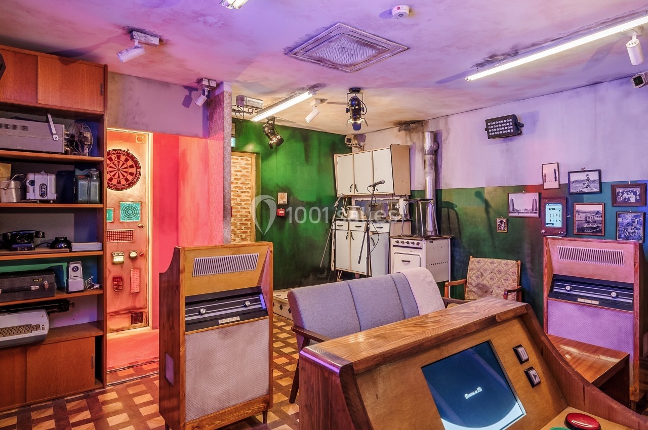 Salle rétro avec mobilier en bois, appareils vintage, fléchettes au mur et éclairage coloré.