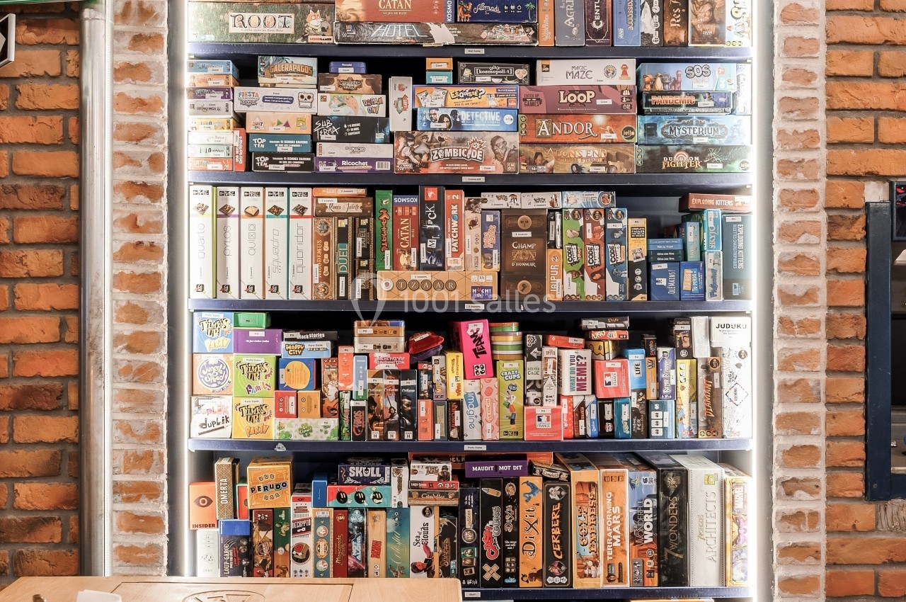 Étagère remplie de jeux de société variés, placée contre un mur en briques dans un espace lumineux.