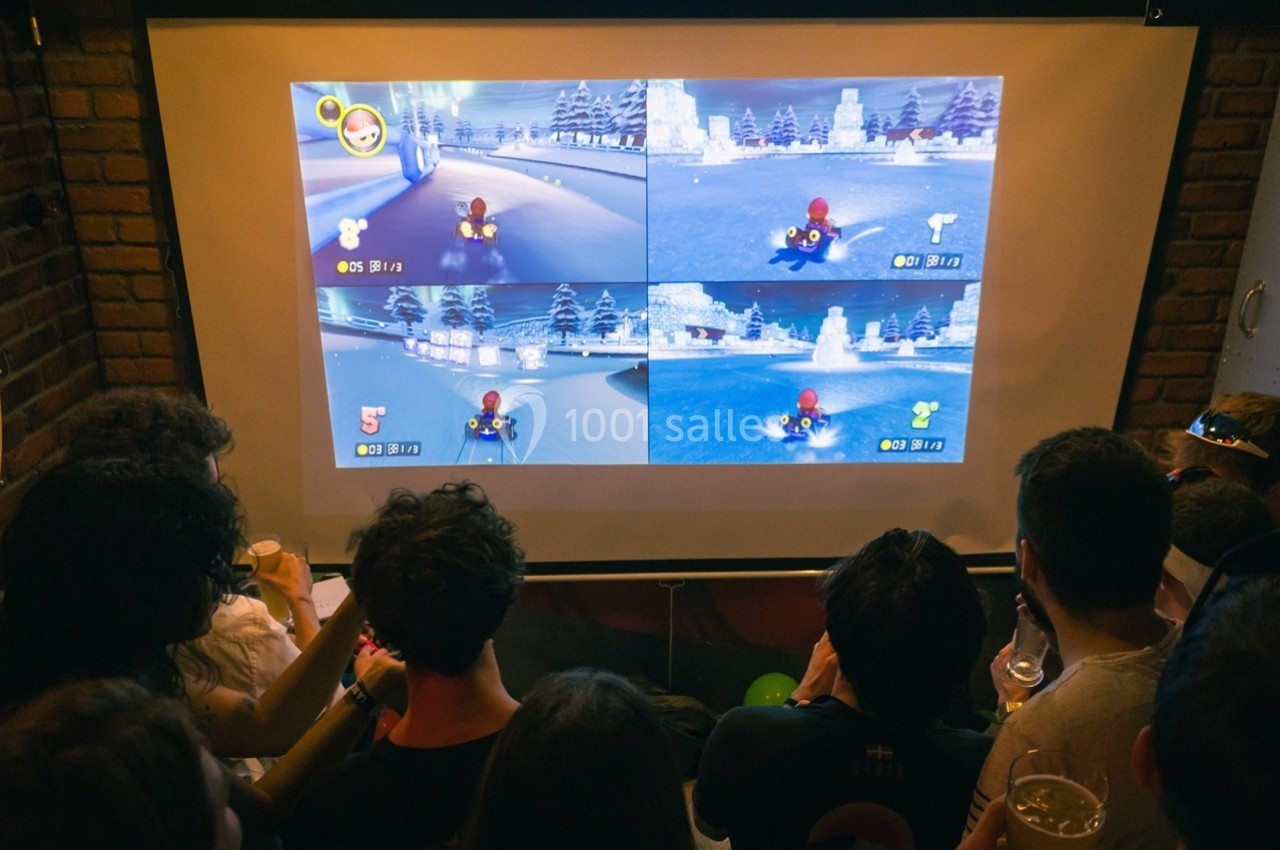 Des personnes regardent un écran projetant une partie multijoueur d'un jeu de course sur quatre sections.