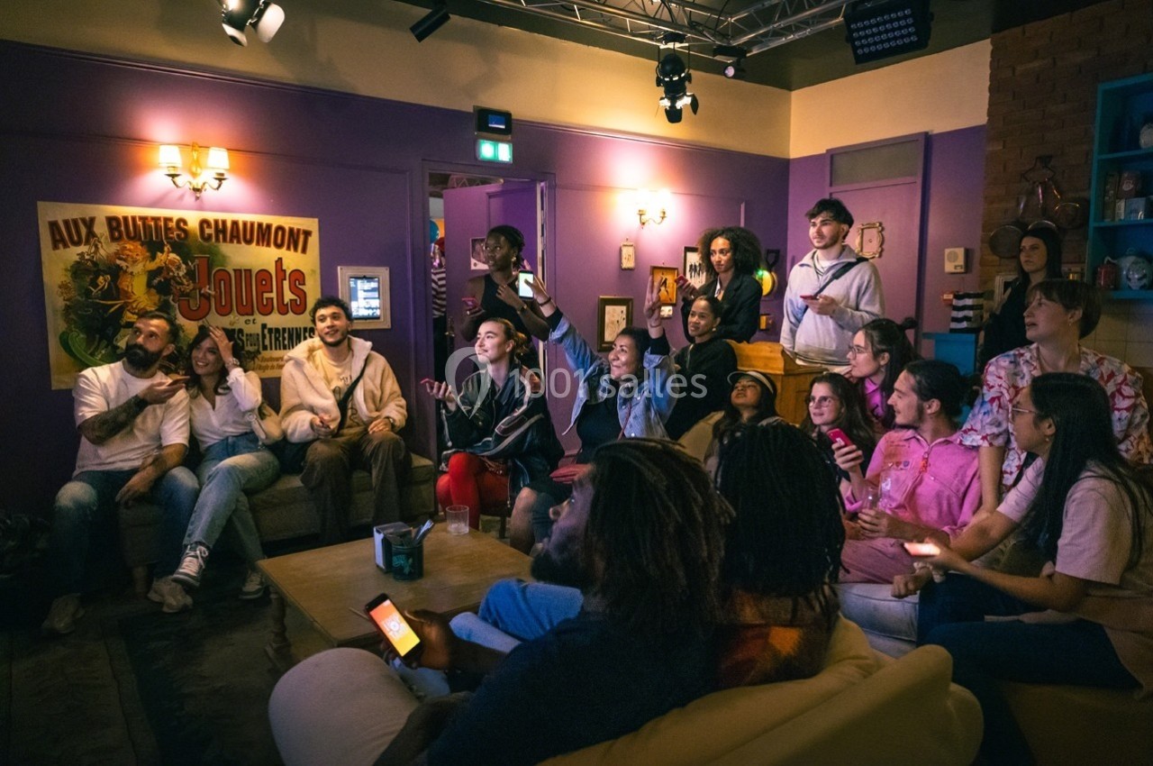 Un groupe de personnes assises et debout dans un salon, regardant un écran hors champ dans une ambiance conviviale.