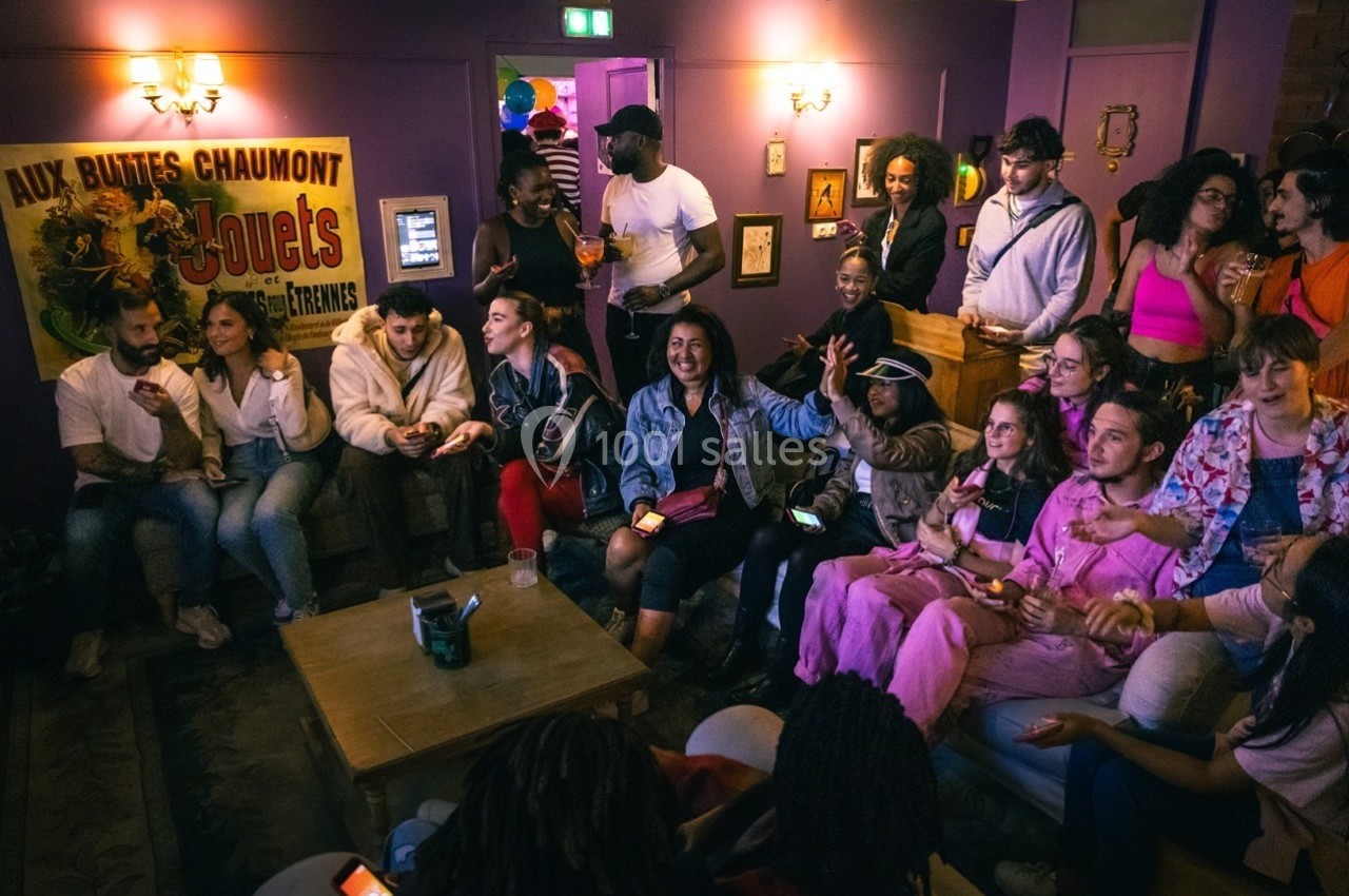 Groupe de personnes assises et debout dans un salon animé, discutant et partageant un moment convivial.