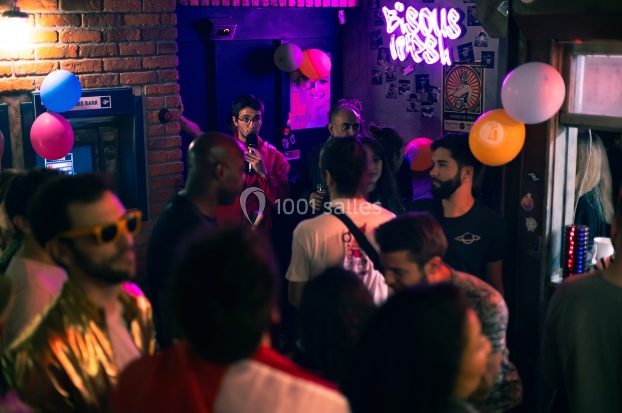 Groupe de personnes dans un bar animé, décoré de ballons et d'une enseigne lumineuse, ambiance festive.