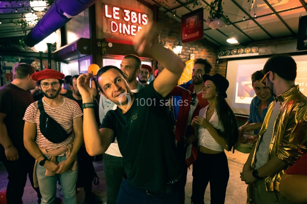 Groupe de personnes dans un diner animé, un homme au premier plan semble danser ou jouer avec énergie.