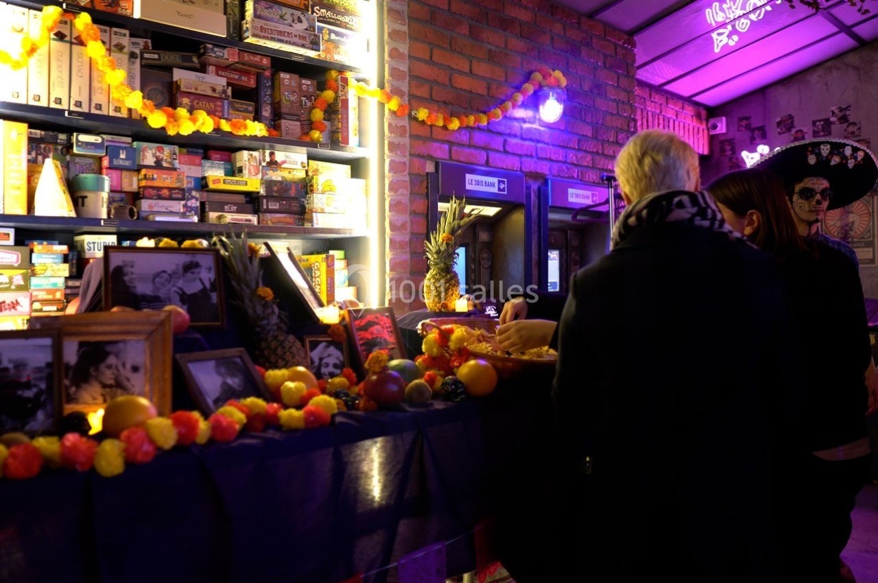 Des personnes devant un comptoir décoré de guirlandes lumineuses, fruits et photos, dans une ambiance tamisée.