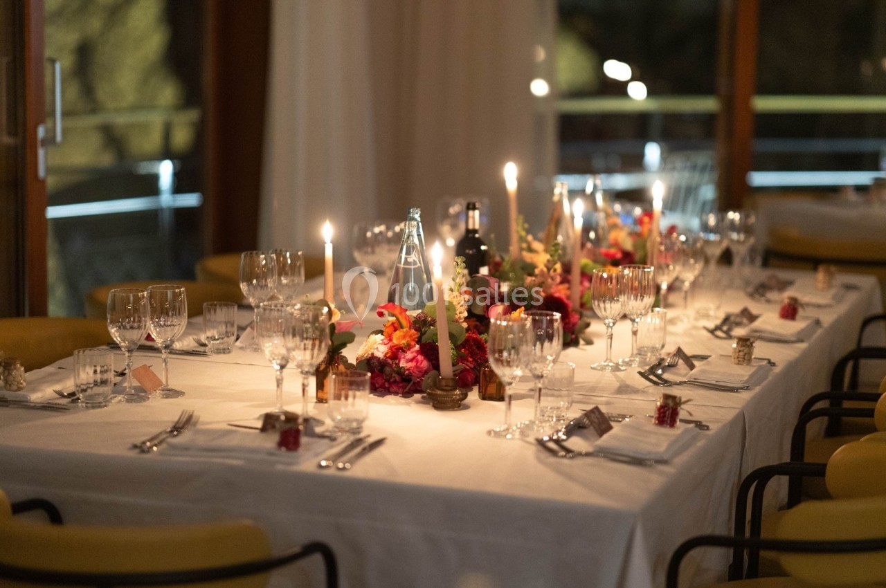 Table élégamment dressée avec bougies, fleurs colorées, verres et couverts dans une ambiance chaleureuse.