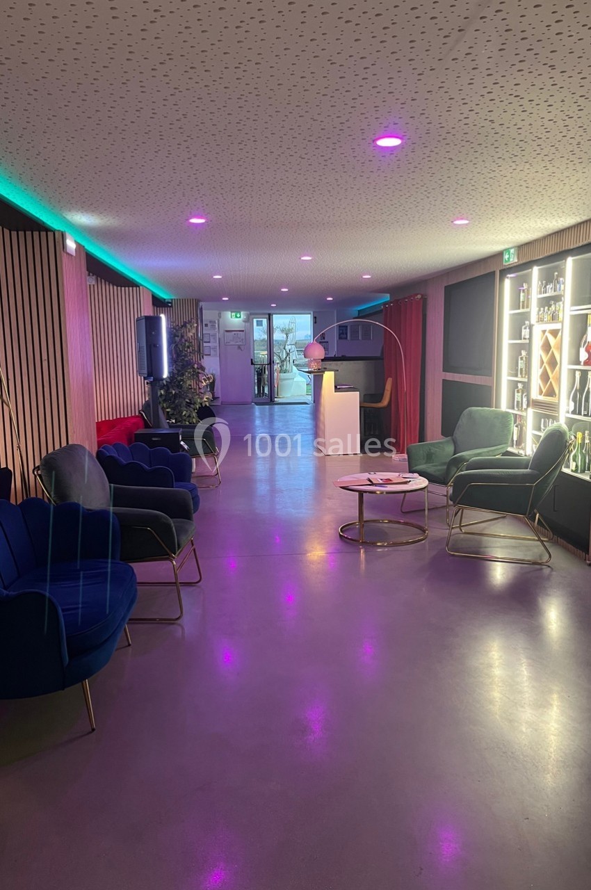 Salon moderne avec fauteuils colorés, éclairage tamisé violet, bar illuminé et décorations élégantes.