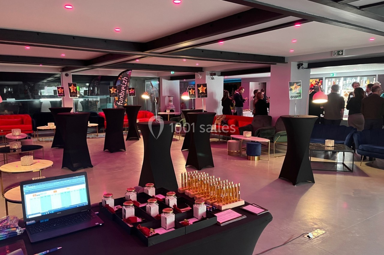 Salle de réception moderne avec tables hautes, canapés colorés, éclairage tamisé et buffet de boissons.