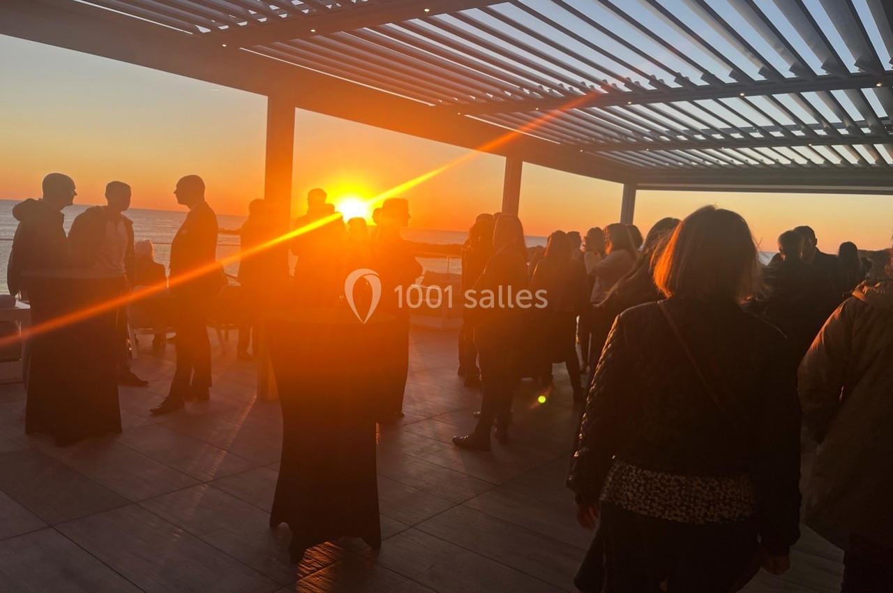 Groupe de personnes discutant sur une terrasse au coucher du soleil, avec une pergola en arrière-plan.