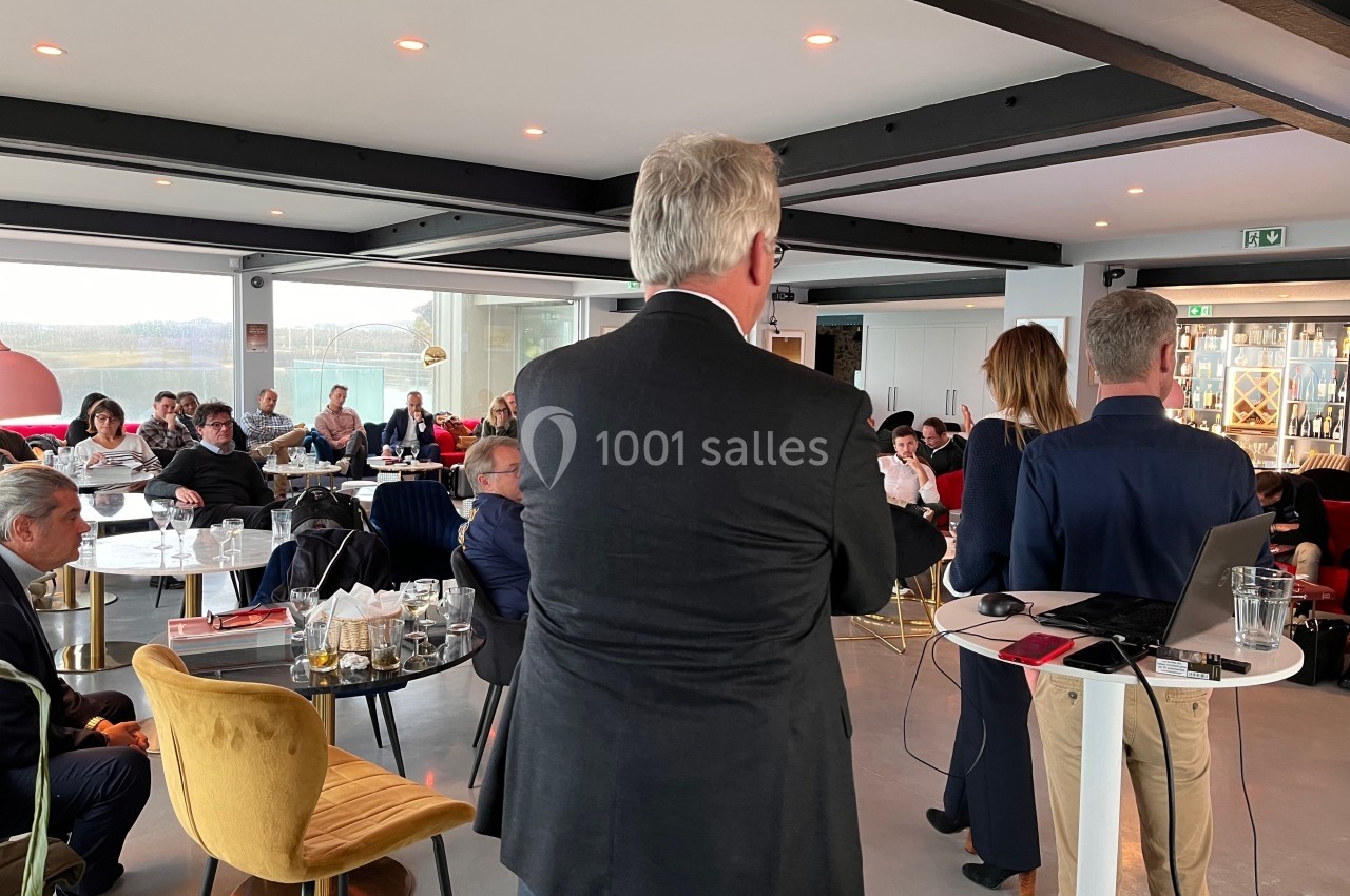 Des personnes assistent à une présentation dans une salle lumineuse avec des tables et des chaises modernes.