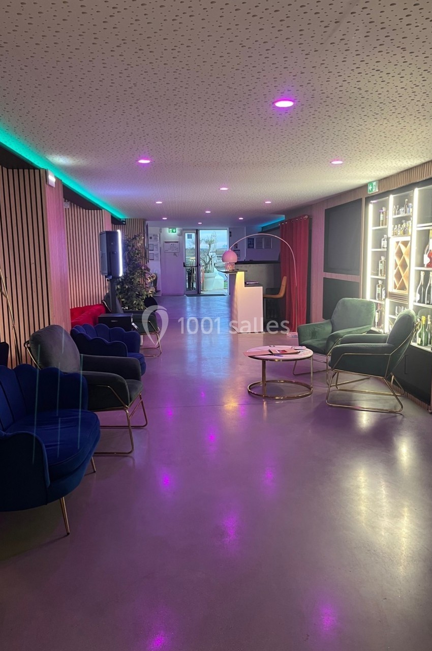 Espace lounge moderne avec fauteuils colorés, éclairage tamisé et étagères illuminées contenant des bouteilles.