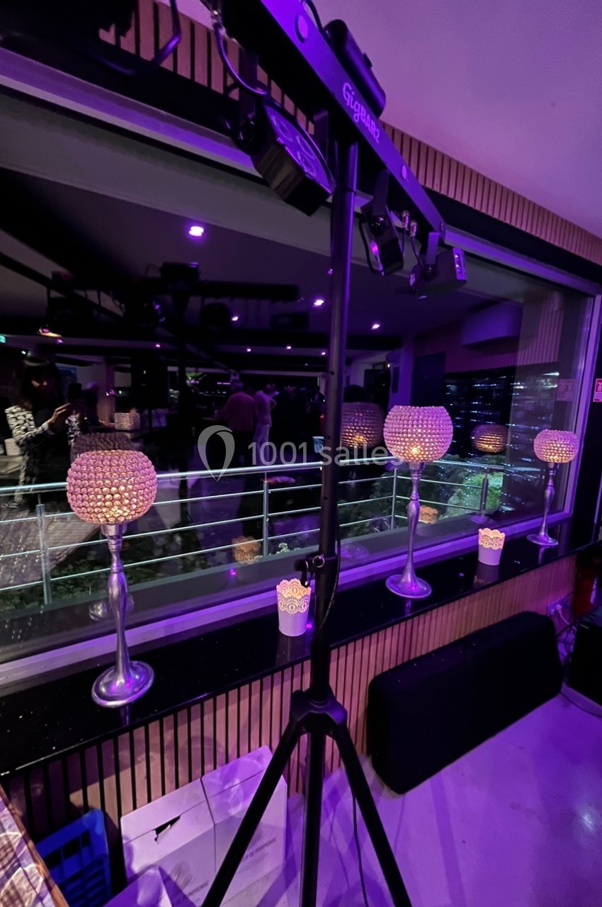Éclairage violet dans une salle avec des bougeoirs décoratifs en cristal et une grande baie vitrée donnant sur la ville.