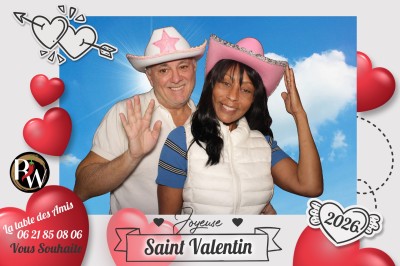 Un couple pose devant une borne photo encadrée, dans un espace élégant avec décor floral et comptoir moderne.