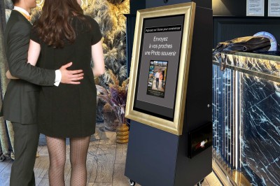 Un couple pose devant une borne photo encadrée, dans un espace élégant avec décor floral et comptoir moderne.