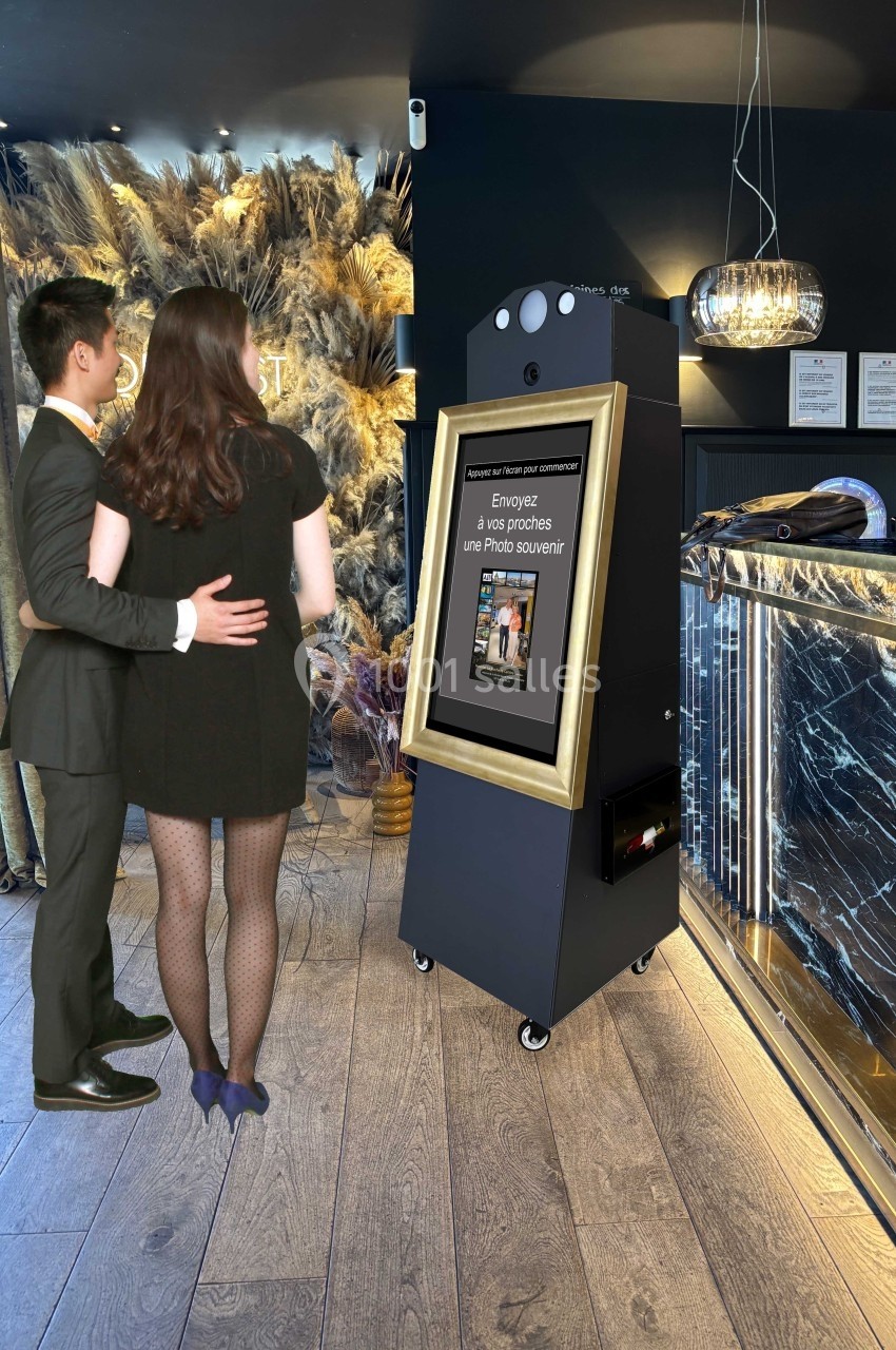 Un couple pose devant une borne photo encadrée, dans un espace élégant avec décor floral et comptoir moderne.