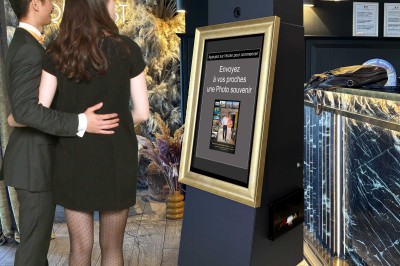 Un couple pose devant une borne interactive permettant d'envoyer une photo souvenir, dans un environnement élégant.