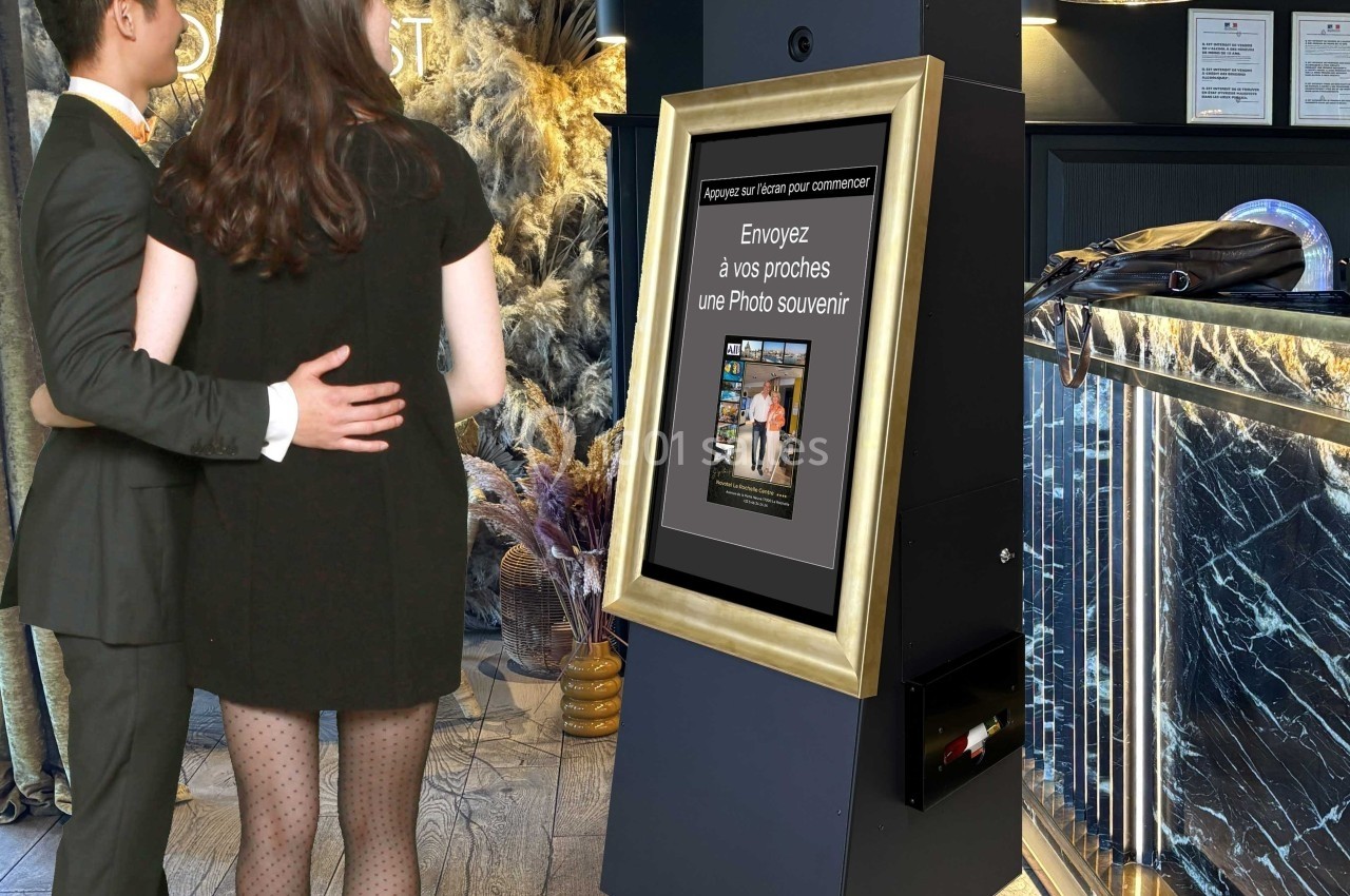 Un couple pose devant une borne interactive permettant d'envoyer une photo souvenir, dans un environnement élégant.