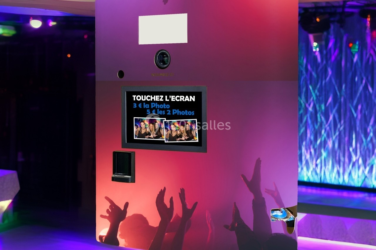 Borne photo interactive avec écran tactile, entourée de lumières colorées et de mains levées dans une ambiance festive.