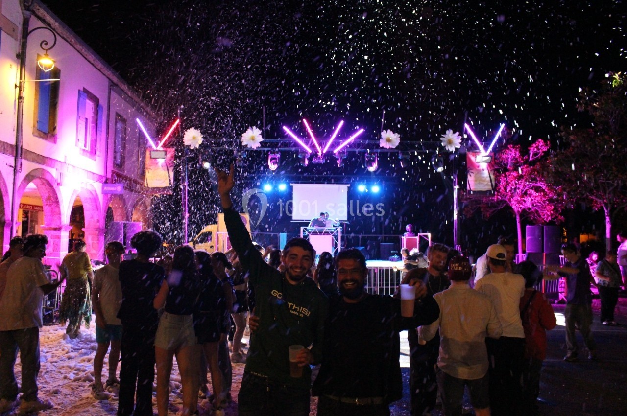 Des personnes dansent et célèbrent sous des lumières colorées et de la mousse lors d'une fête nocturne en extérieur.