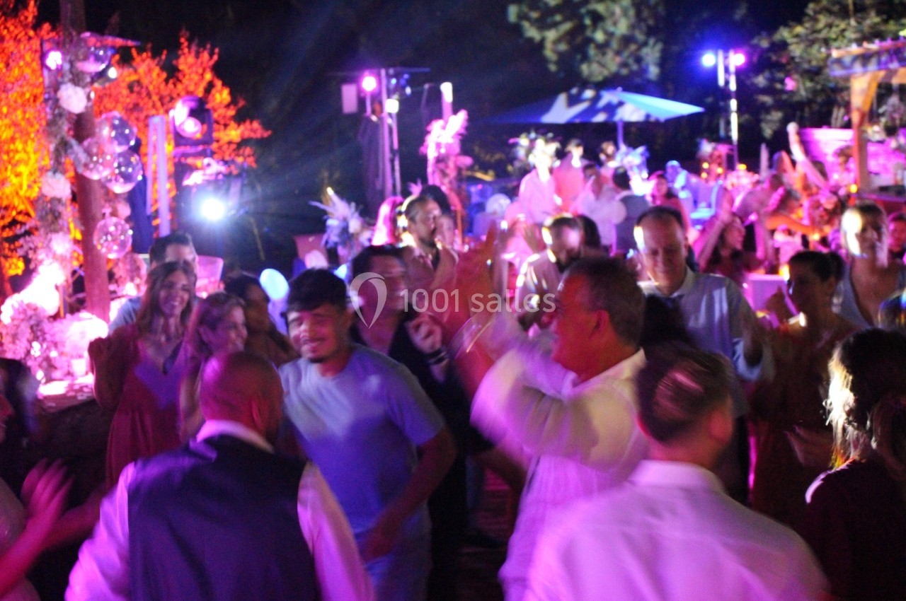 Groupe de personnes dansant et célébrant en soirée, éclairées par des lumières colorées dans une ambiance festive.