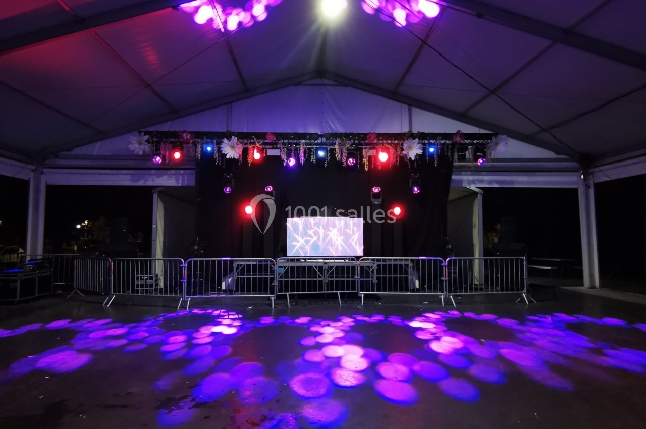 Scène sous chapiteau avec éclairage violet et rose, barrière de sécurité et écran central en arrière-plan.