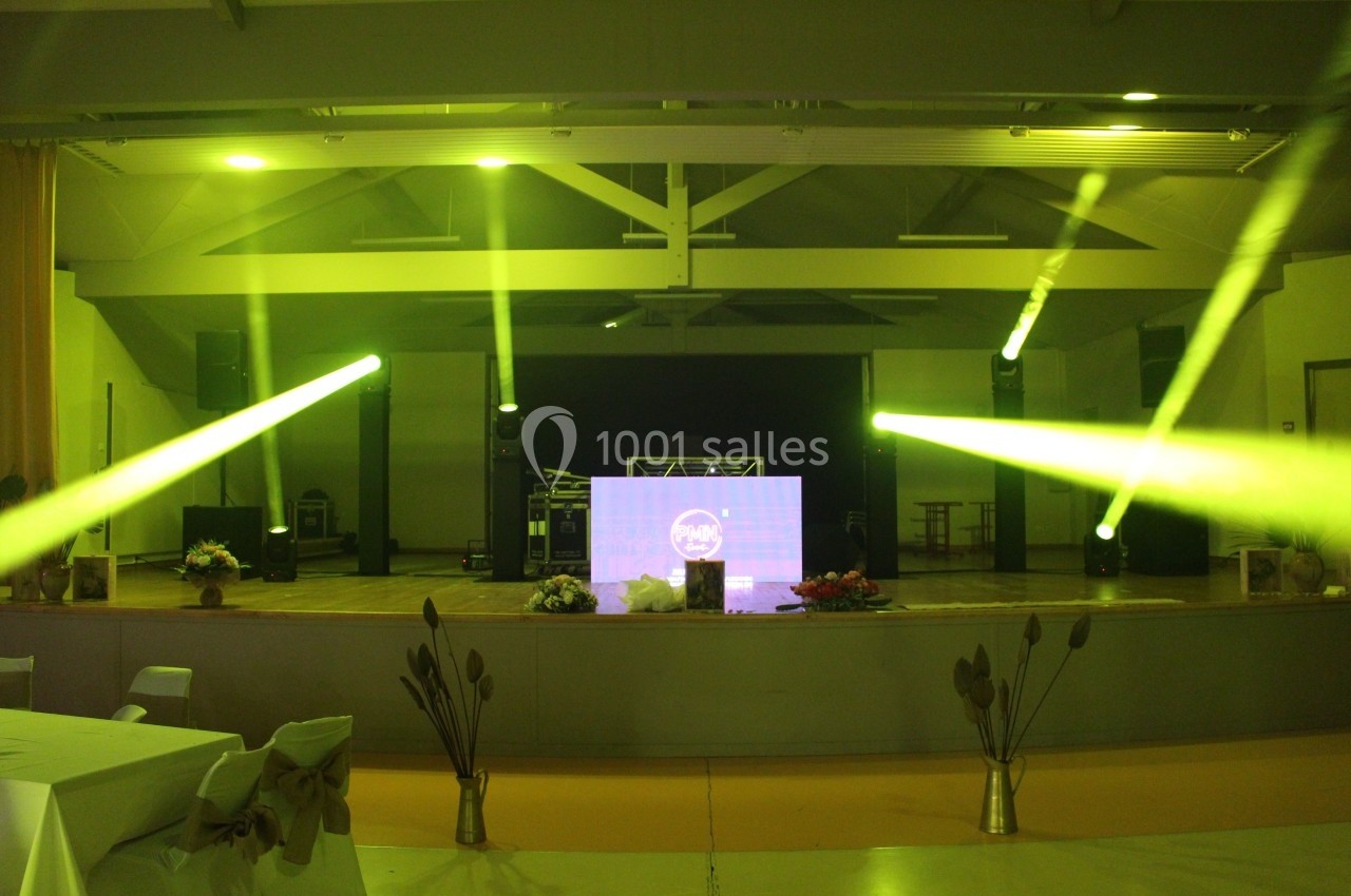 Scène de salle de réception illuminée par des projecteurs jaunes, avec une table de mixage et des décorations florales.