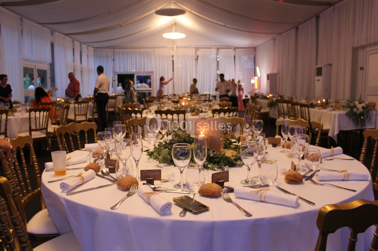 Salle de réception décorée pour un dîner, avec tables rondes dressées, nappes blanches et éclairage chaleureux.