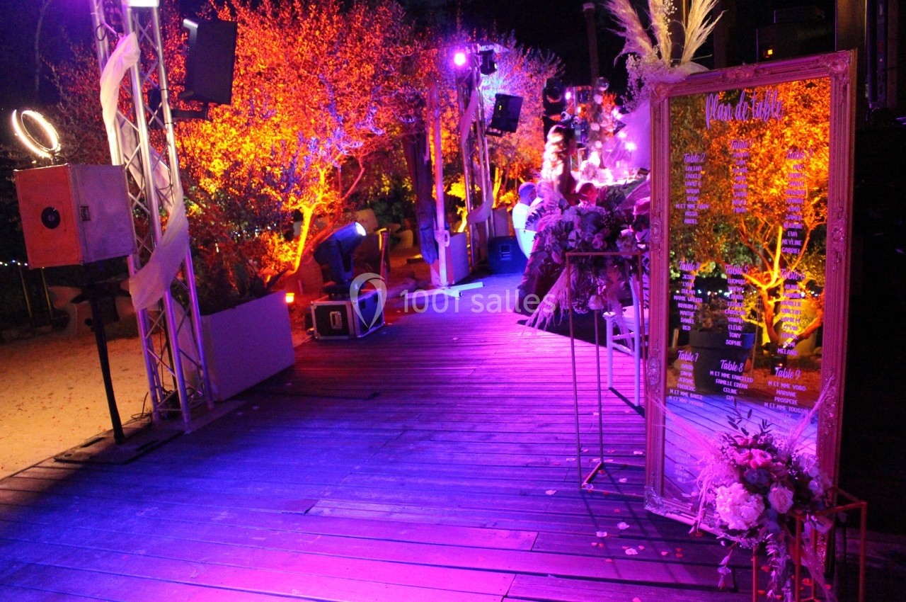 Décoration de soirée en extérieur avec éclairages colorés, cadre doré et fleurs sur une terrasse en bois.