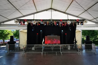 Scène couverte avec une table de mixage, des enceintes et une décoration florale, entourée de barrières de sécurité.