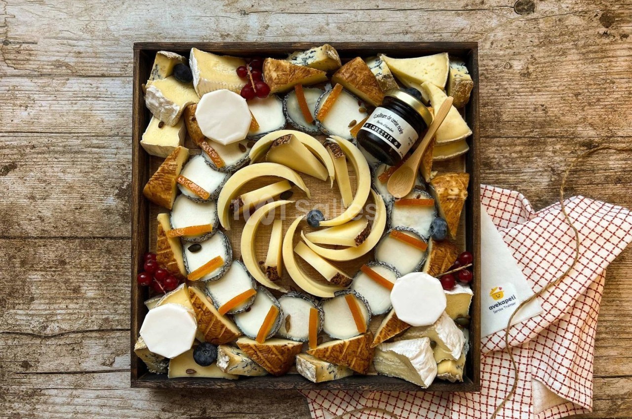 Plateau de fromages variés avec fruits, confiture et crackers, présenté sur une table en bois avec une serviette à carreaux.
