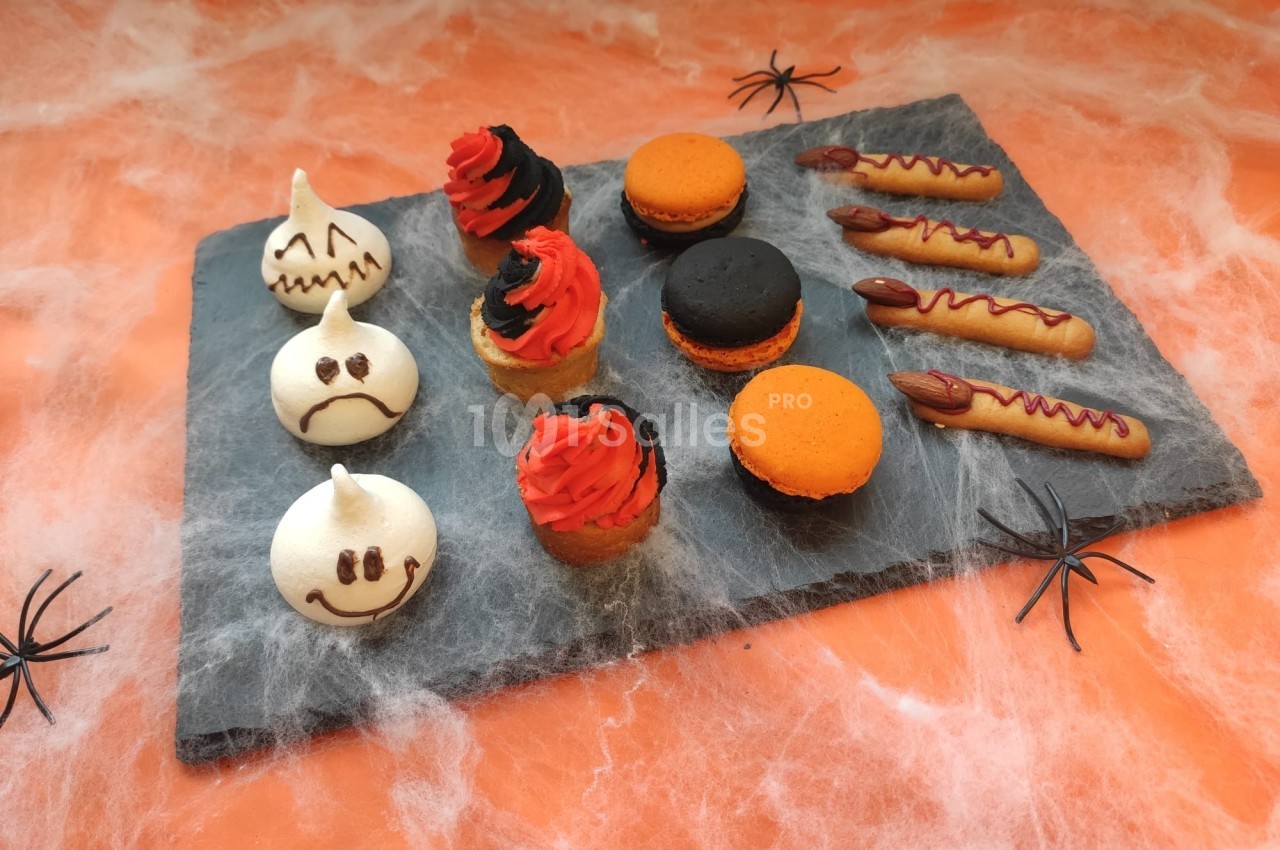Plateau d'Halloween avec meringues décorées, cupcakes, macarons orange et noir, et biscuits en forme de doigts.