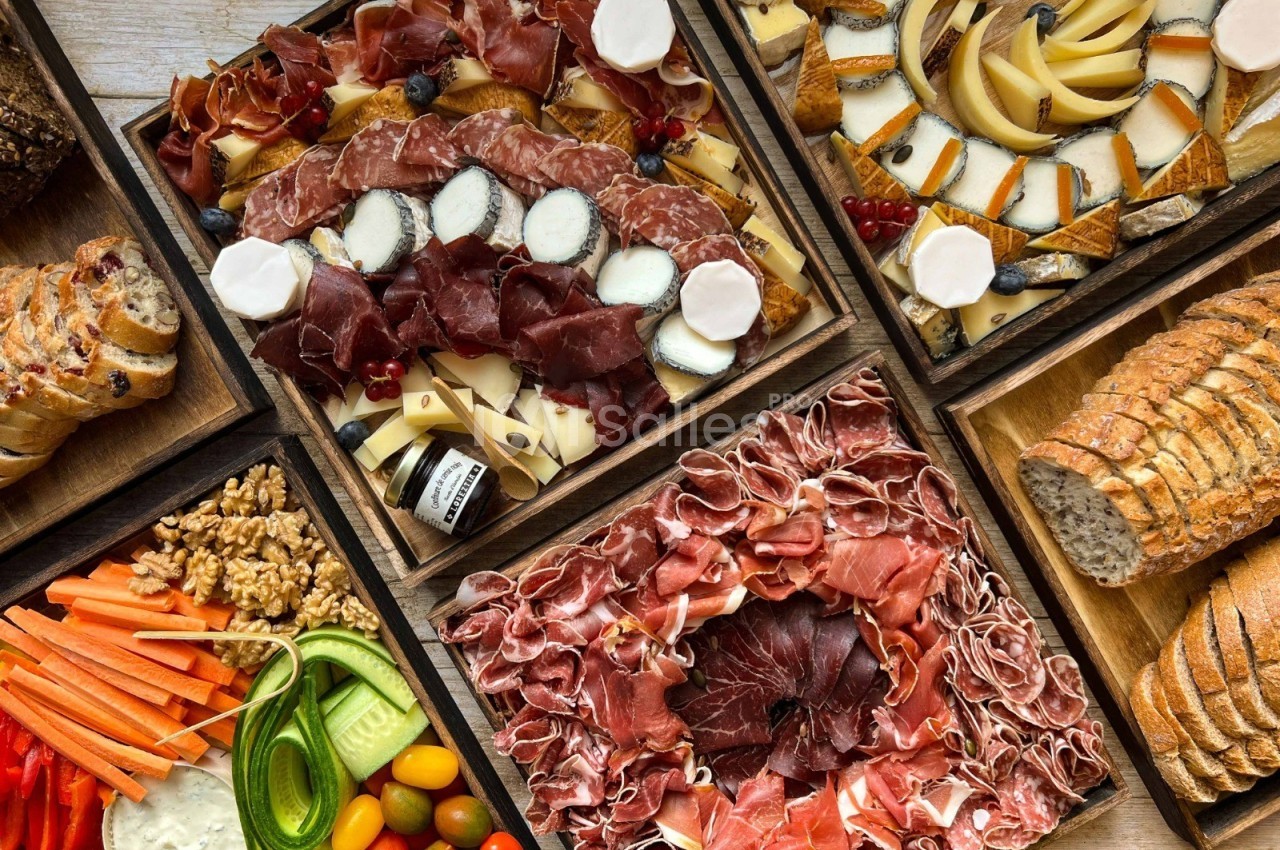 Plateaux variés de charcuterie, fromages, légumes frais, fruits secs et pains disposés sur une table en bois.