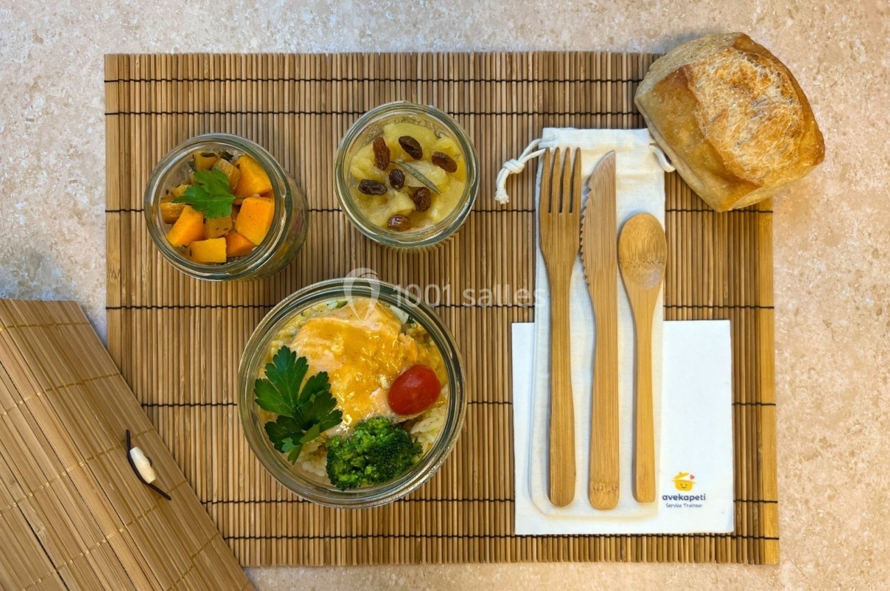 Repas présenté sur un set en bambou avec bocaux contenant légumes, purée, œuf, pain et couverts en bois.