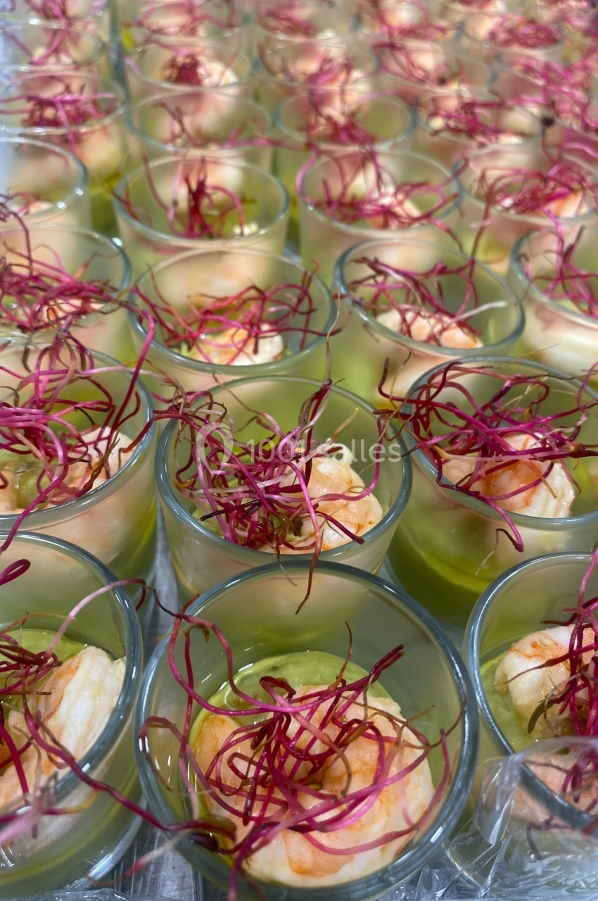 Verrines de crevettes sur lit de purée verte, garnies de pousses rouges, disposées en rangées.